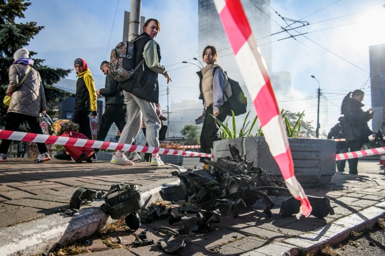 Young women look at the smouldering remains of a drone on a Kyiv street surrounded by police tape.