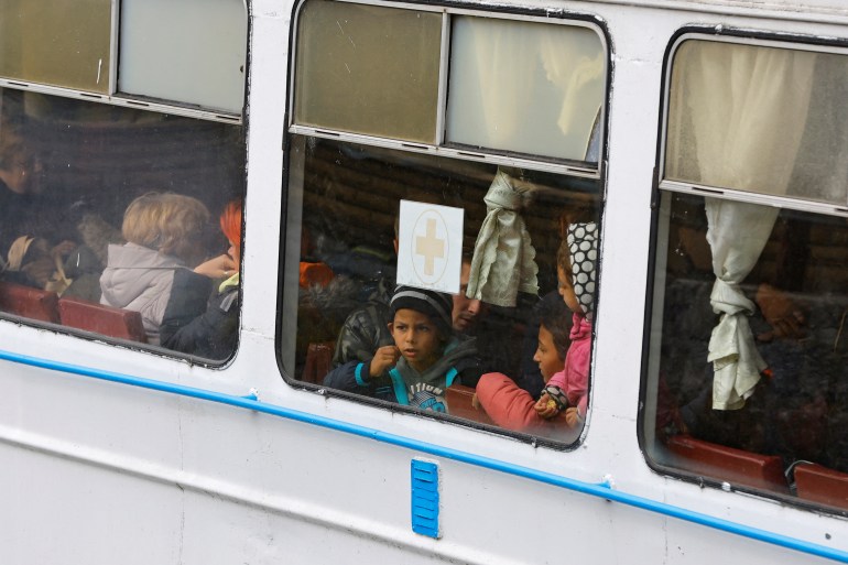 A boy looks out one of three windows of a train, which show scores of passengers