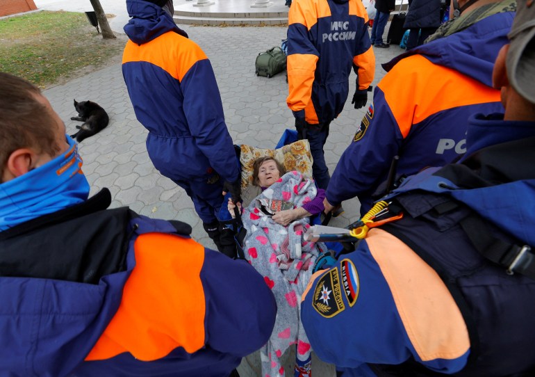 Members of the Russian Emergencies Ministry carry an elderly woman evacuated from the Russian-controlled city of Kherson, in the town of Oleshky, Kherson region, Russian-controlled Ukraine October 22, 2022