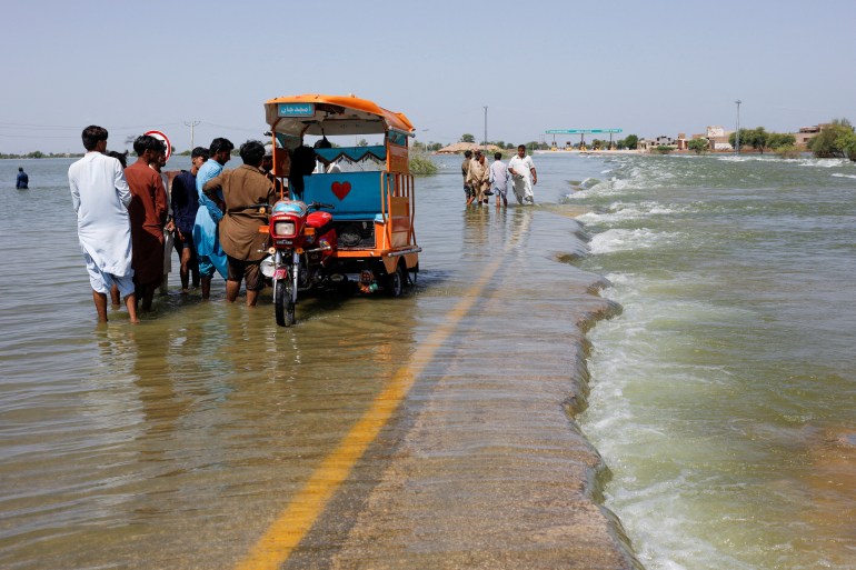 Displaced people stand on flooded highway in Pakistan.