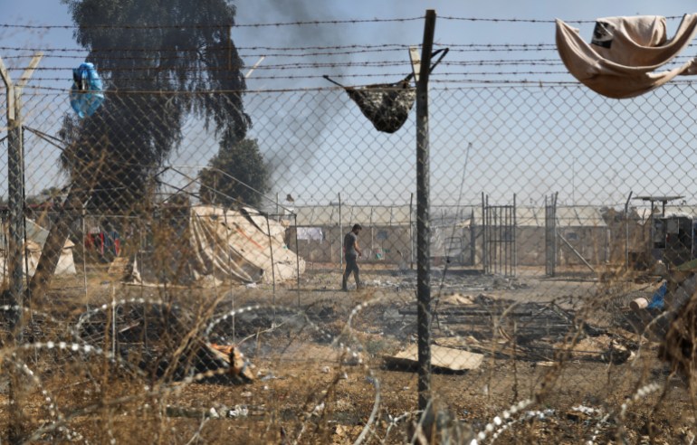 A migrant walks next to burned tents in the Pournara refugee camp during clashes in Kokkinotrimithia, on the outskirts of Nicosia