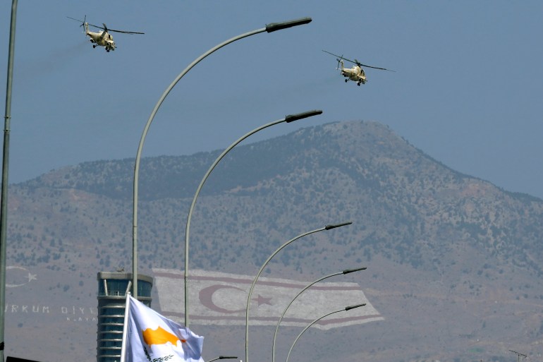 Military helicopters of Cypriot air forces fly over a military parade marking the 62nd anniversary of Cyprus' independence from British colonial rule, as the giant paintings of the Turkish and the Turkish Cypriot breakaway flags are seen on Pentadahtilos mountain in the Turkish occupied area in the background, in Nicosia, Cyprus
