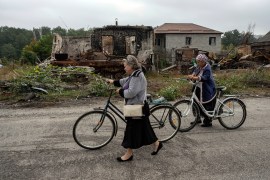 Women walk on a street near destroyed Russian APC and destroyed houses in the recently liberated town of Sviatohirsk [Evgeniy Maloletka/AP]