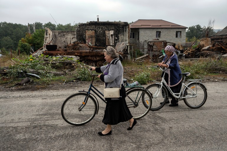 Women walk on destroyed street.