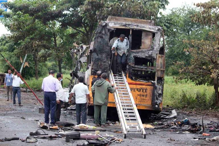 People inspect a bus that caught fire in a highway in Nashik