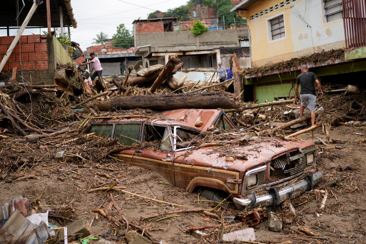 A car almost buried in piles of wet mud with destroyed buildings behind after a landslide in Las Tejerias, Venezuela.