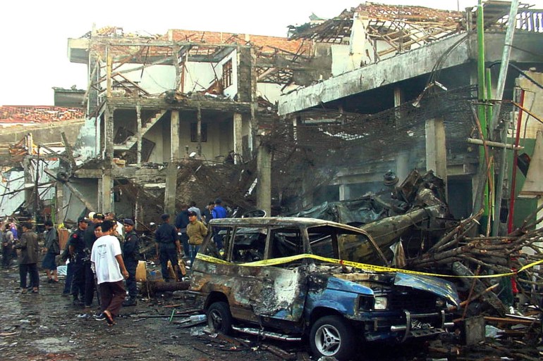 A police officer inspects a burnt-out vehicle, dilapidated buildings and debris after the 2002 Bali attacks.