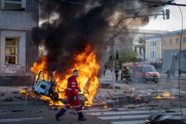 A medical worker runs past a burning car after a Russian attack in Kyiv