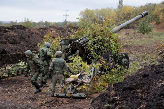 Ukrainian soldiers in green uniforms preparing to fire from howitzer, which is covered in greenery
