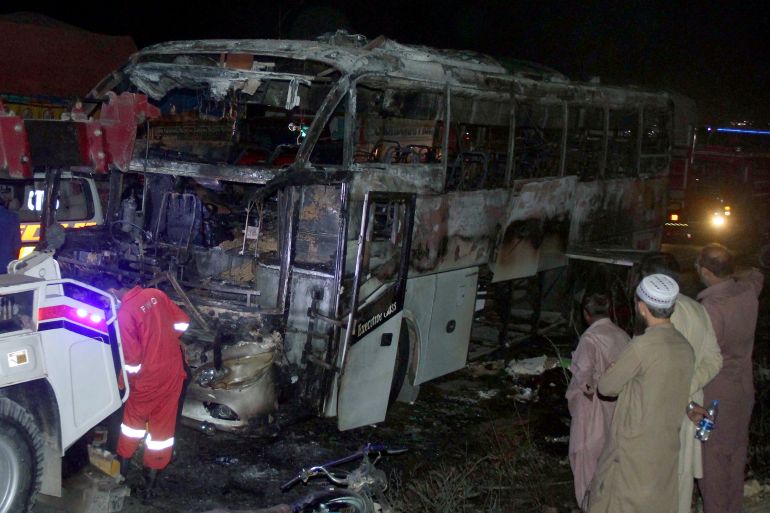 Volunteers gather beside a charred bus on a highway in Nooriabad, Pakistan