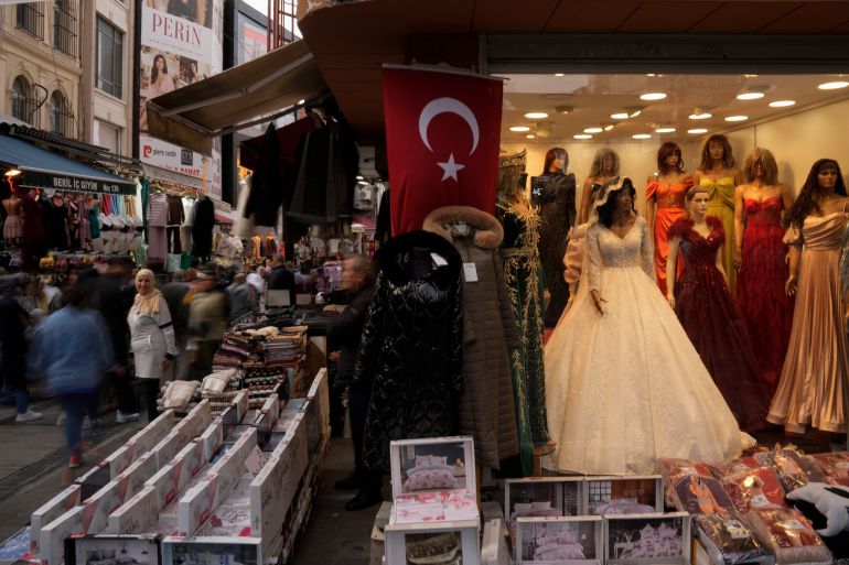 People walk past clothes shops; one has wedding dress on display