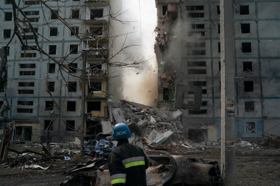 A firefighter looks at a part of a wall falling in the middle of a grey apartment bloc with blown out windows