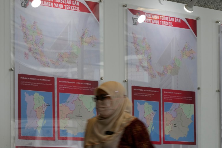 A member of the Election Commission staff walks past a board showing maps of small and large constituencies