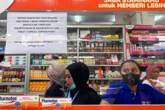 Pharmacy employees in Jakarta, Indonesia, wait for customers at a counter displaying a notification saying that the sale of medicinal syrup is temporarily halted on October 20, 2022 [Tatan Syuflana/AP]