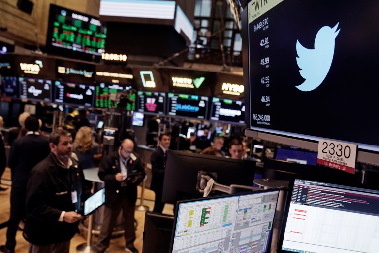 The symbol for Twitter appears above a trading post on the floor of the New York Stock Exchange as brokers take notes.