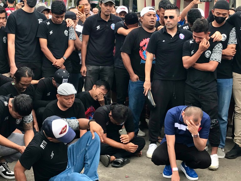 Members of the Arema football club break down and cry at a shrine built in the car park of Kanjuruhan Stadium during a commemorative service on October 3. 2022 [Al Jazeera]
