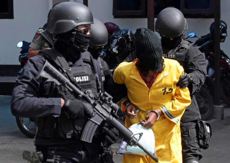 Armed Densus 88 officers escort a prisoner in a yellow jumpsuit to Jakarta