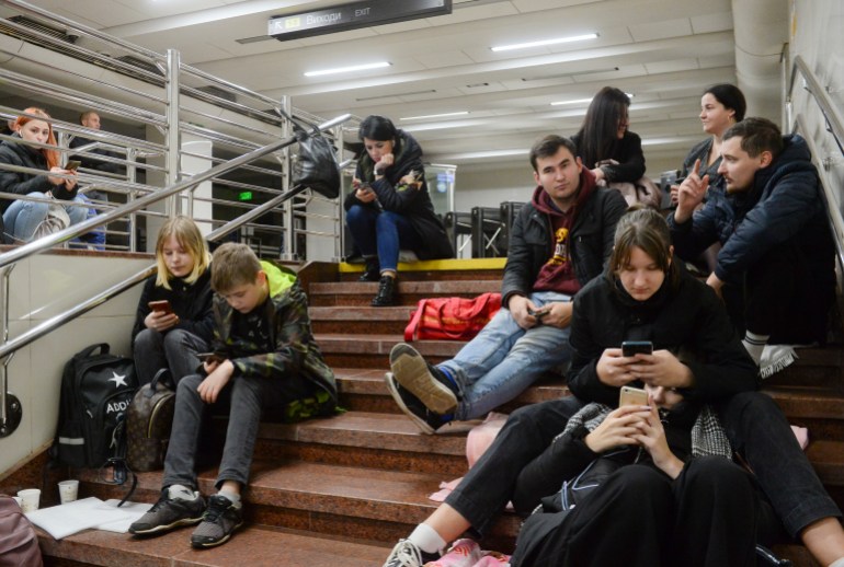 People check their phones as they shelter inside a metro station after Russian shelling in Kyiv