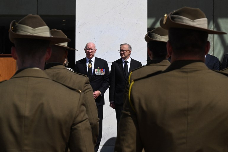 Backs of two rows of soldiers, with Albanese and Hurley standing in the middle, in front.
