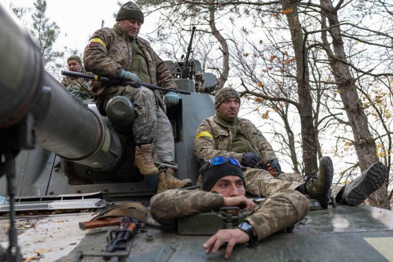 Ukrainian soldiers sitting on top of a tank in a wooded area as they prepare to fire at Russian positions in Kherson