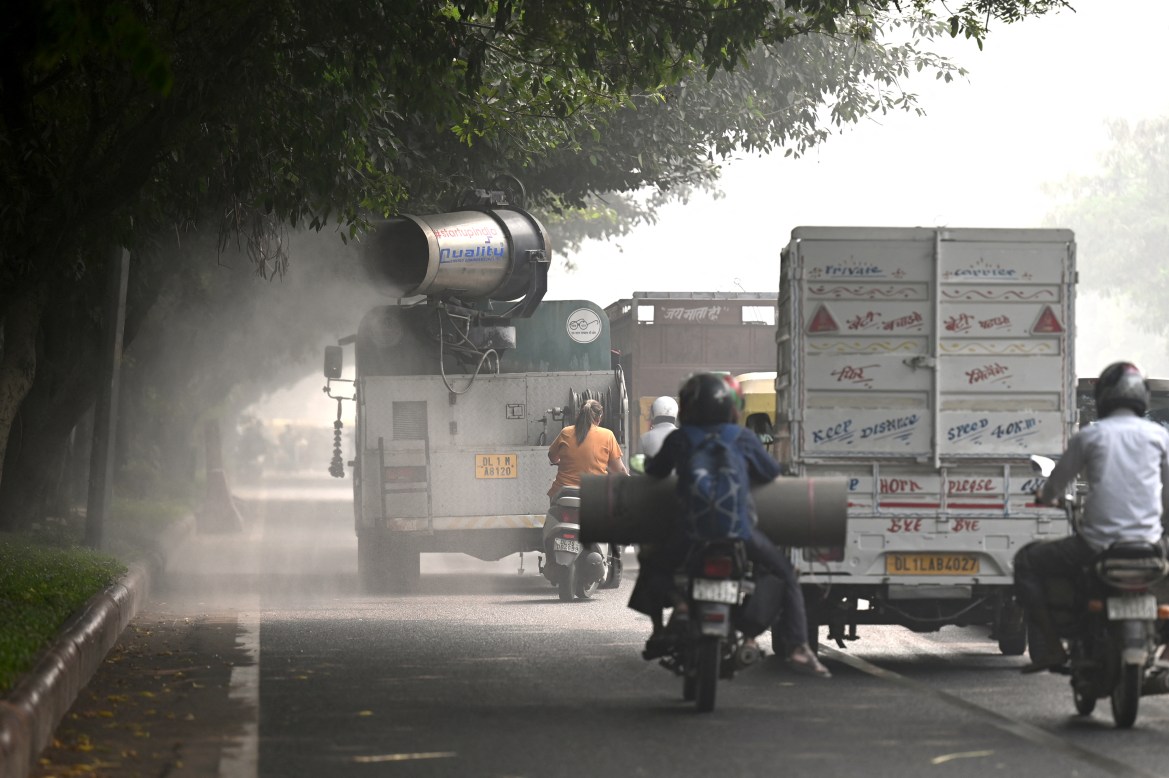 Commuters ride past an anti-smog gun spraying water to curb air pollution amid heavy smog conditions in New Delhi.