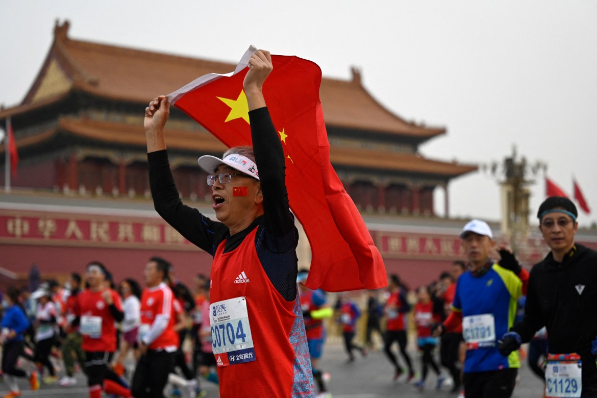 A participant holding a Chinese national flag runs past Tiananmen Square during the Beijing Marathon