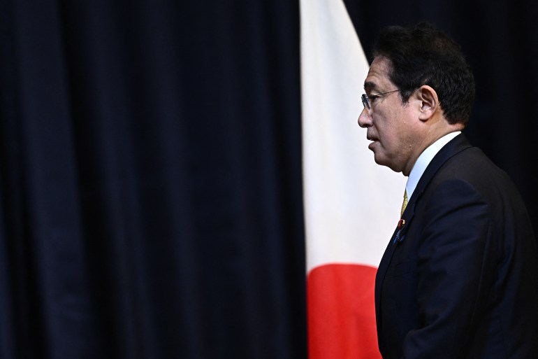 Japanese PM in a suit walks past a Japanese flag at a press conference during the Asia-Pacific Economic Cooperation summit in Bangkok, Thailand.