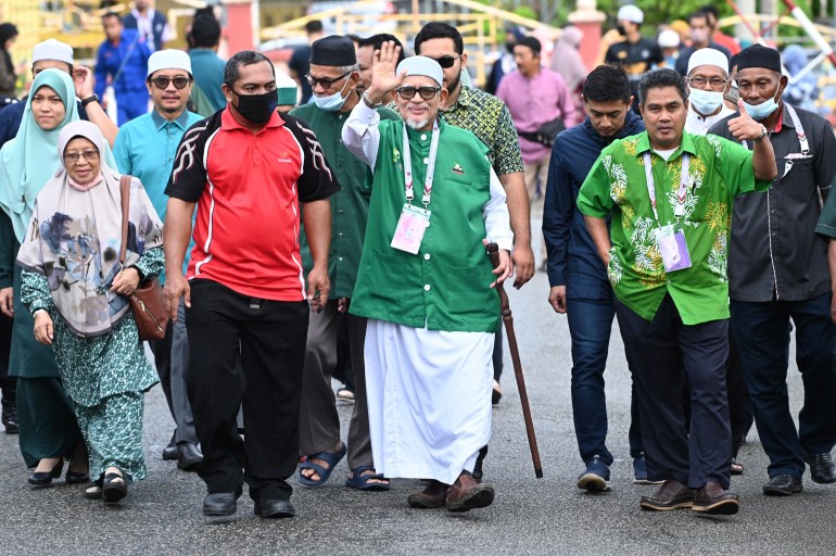 (PAS) leader Abdul Hadi Awang, dressed in his party green and white robes, smiles and waves