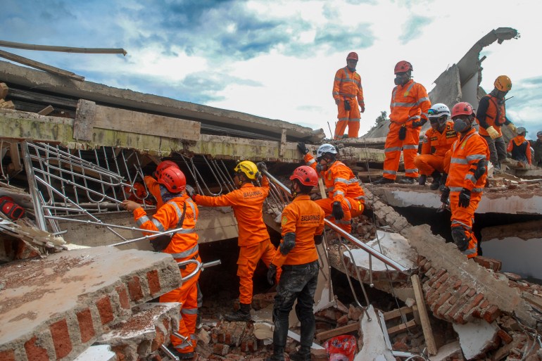 Rescuers in orange uniforms standing on front of an on top of a collapsed building