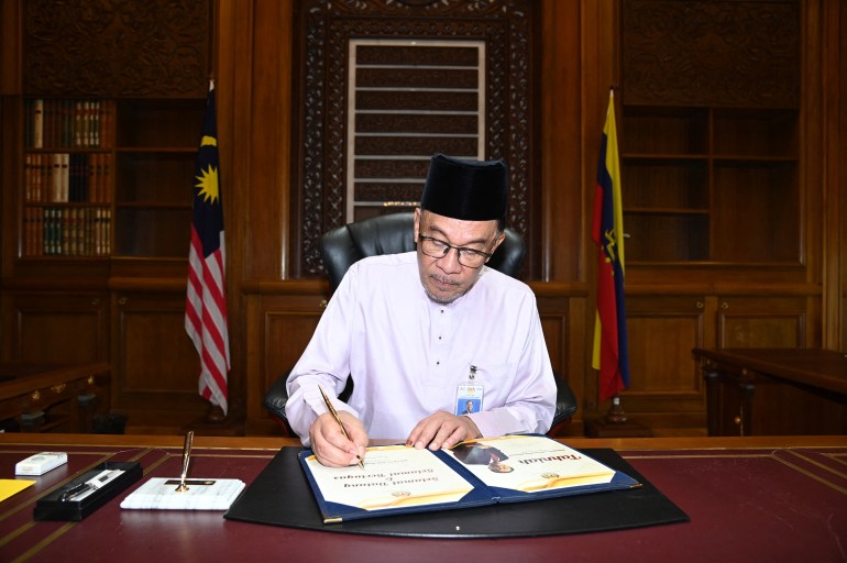 Anwar in white shirt and black songkok in the prime minister's office signing documents