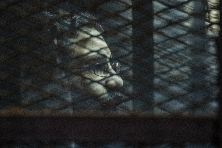 Egyptian activist Alaa Abdel Fattah stands behind bars with fellow defendants during their verdict at a police institute in Cairo's Tora prison on February 23, 2015.