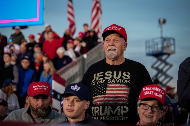 Trump supporter in Ohio wearing a red baseball cap and black-t-shirt reading 'Jesus is my saviour, Trump is my president' with an image of an American flag.