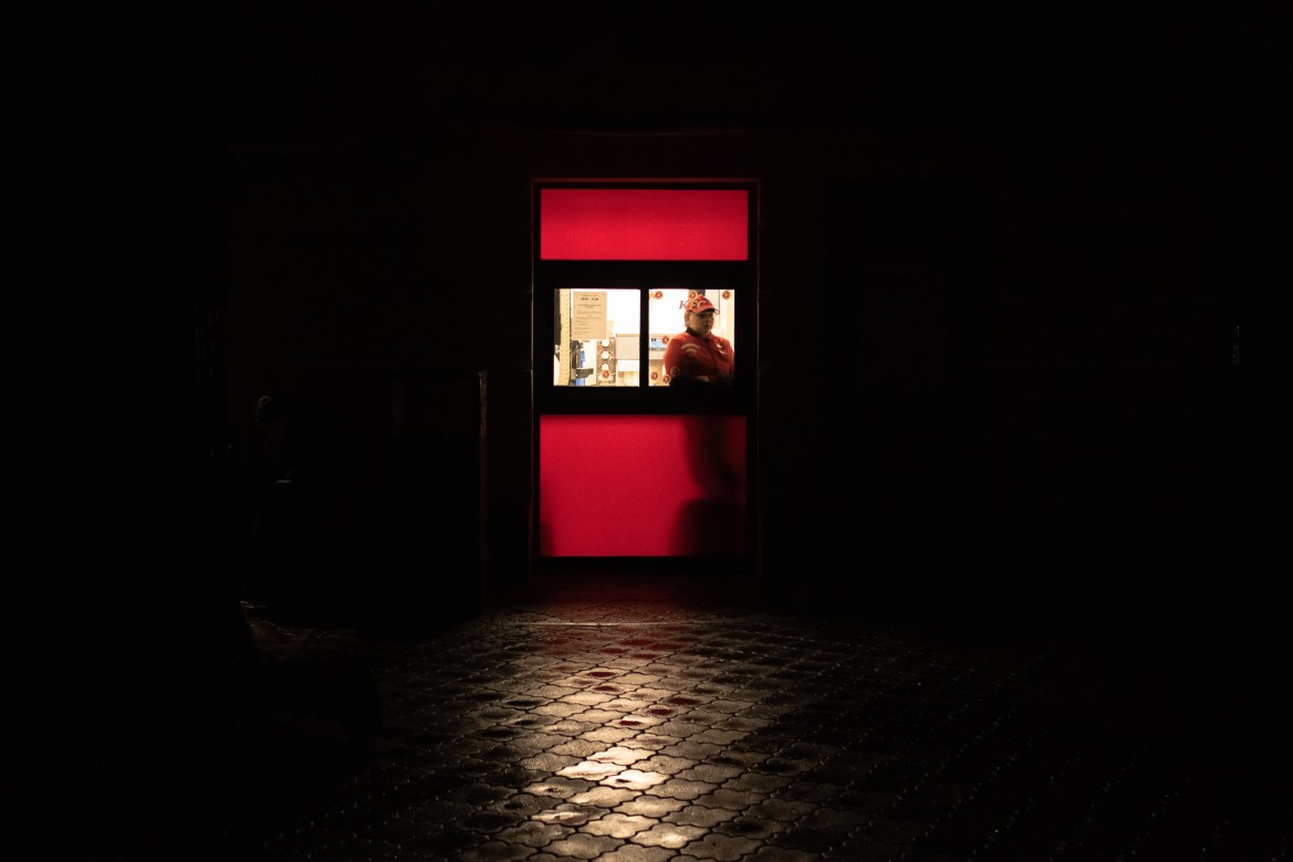 A worker of a fast food restaurant waits for customers at a non-illuminated street.