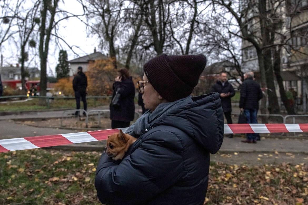 A woman holding a dog stands behind a police line next to a residential building that was hit during a Russian attack