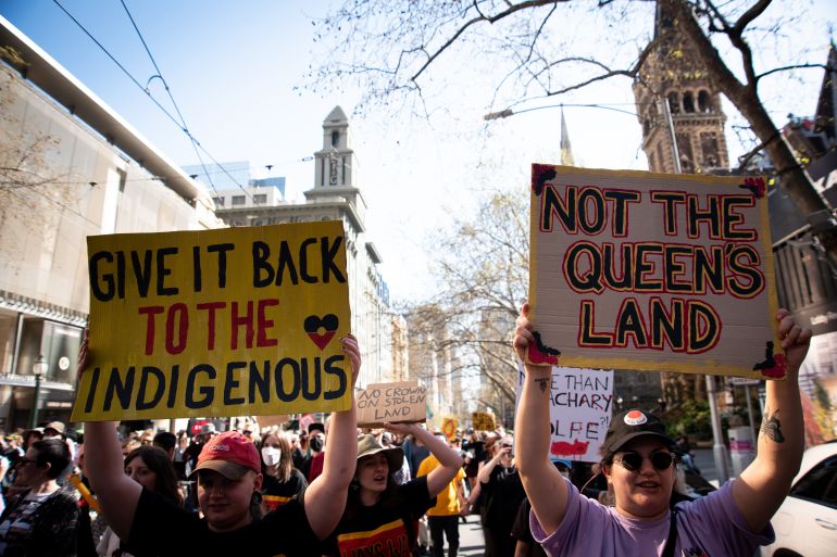 Protesters carrying signs saying 'not the queen's land' and 'give it back to the indigenous' at a rally in Melbourne