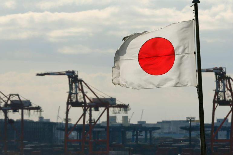A Japanese flag flutters in front of a shipping container area, at a port in Tokyo, Japan.