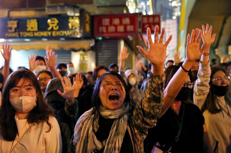 Young women hold five fingers aloft and sing Glory to Hong Kong at a nigthtime protest in Hong Kong in 2019.