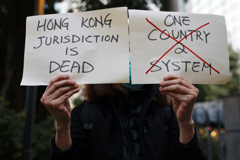 A protester holds up two face shields.  One says Hong Kong's jurisdiction is dead and the other shows the words one country, two systems with a big red cross through them 