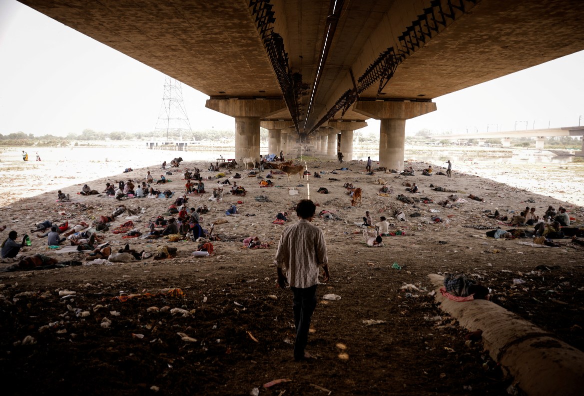 People sleep on the Yamuna river bed under a bridge on a hot summer day