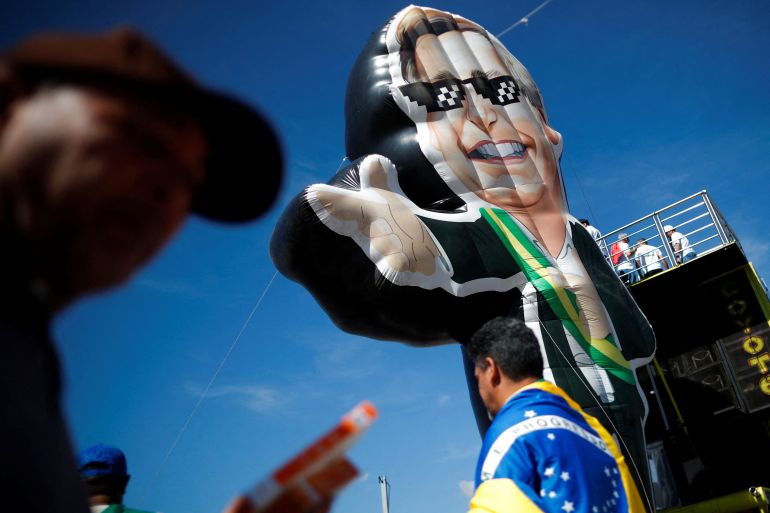 large inflated doll with the top half of a man draped in a Brazillian flag walking underneath