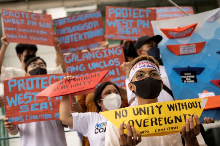 Maske takan ve Filipinler'in Güney Çin Denizi'ndeki iddiasını destekleyen pankartlar tutan protestocular