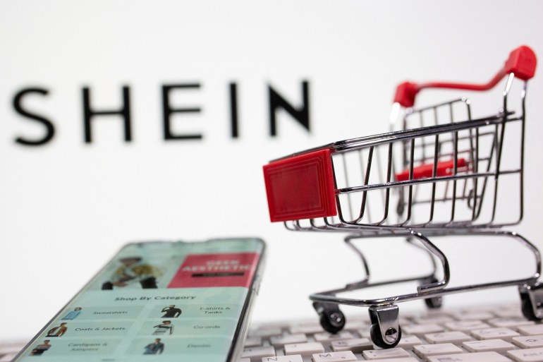 A keyboard and a shopping cart are seen in front of a displayed Shein logo