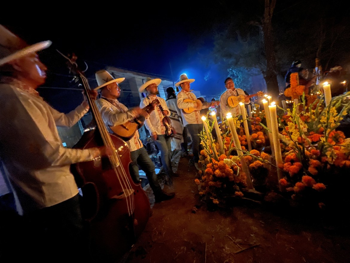 Musicians play their instruments around a grave