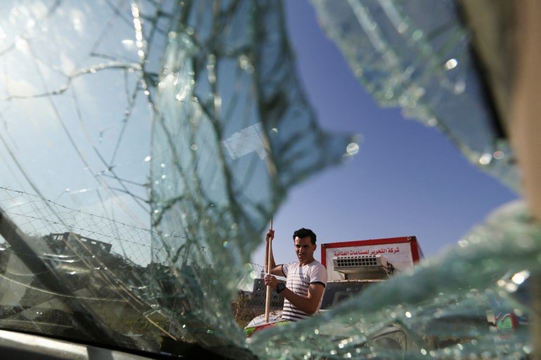 A Palestinian man is seen through a shuttered window of a car near an Israeli airstrikes