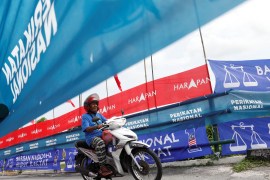 A man on a motorbike drives alongside flags over Malaysia's three main coalition groupings during the 2022 election campaign