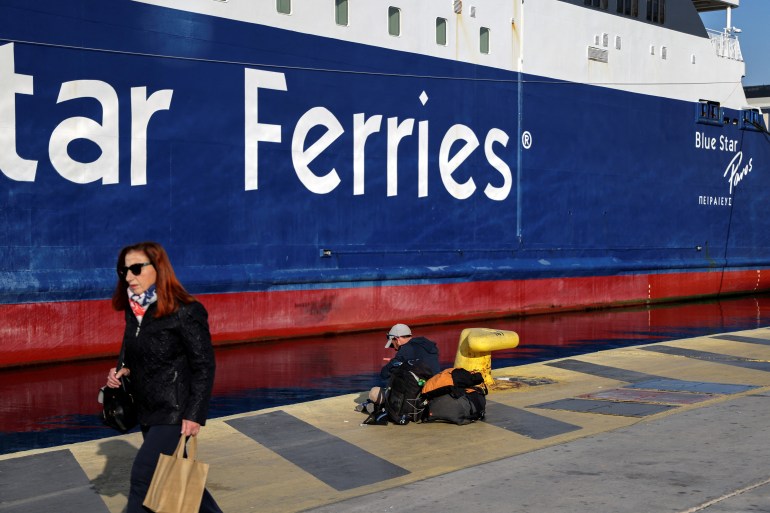 A man sits next to a moored passenger ferry as a woman walks by, during a 24-hour general strike at the port of Piraeus, Greece