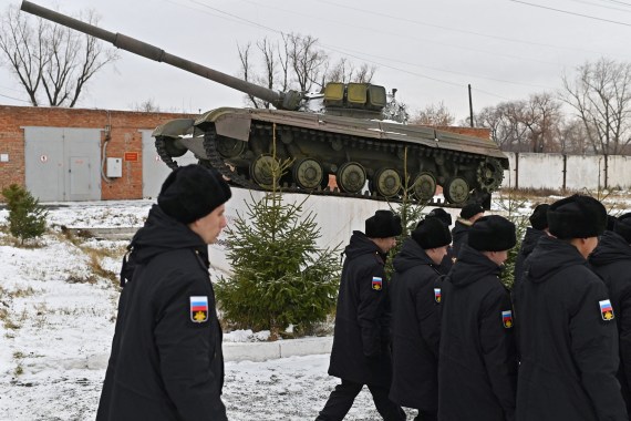 Russian conscripts in winter uniform walk on snow, there is a tank behind them