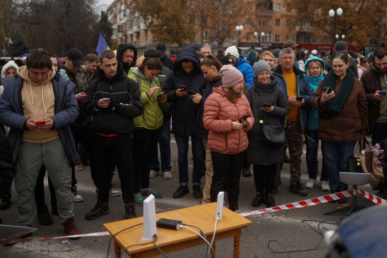 Kışlık giysiler içindeki insanlar, cep telefonu kapsama alanına girmek ve aileleriyle konuşmak için bir uydu bağlantısının etrafında toplandı.