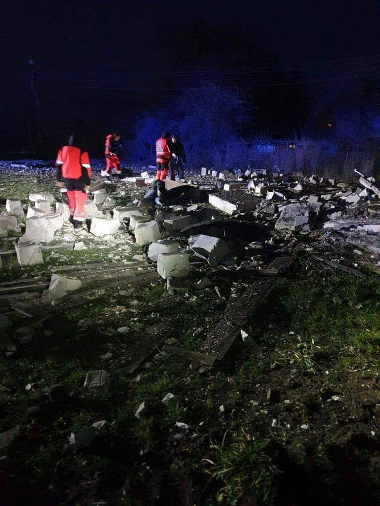 Night time scene showing damage at the site of an explosion in a village in Poland with rescue workers standing in the rubble