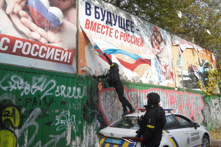 Ukrainian police officers rip Russian propaganda billboards off in the city